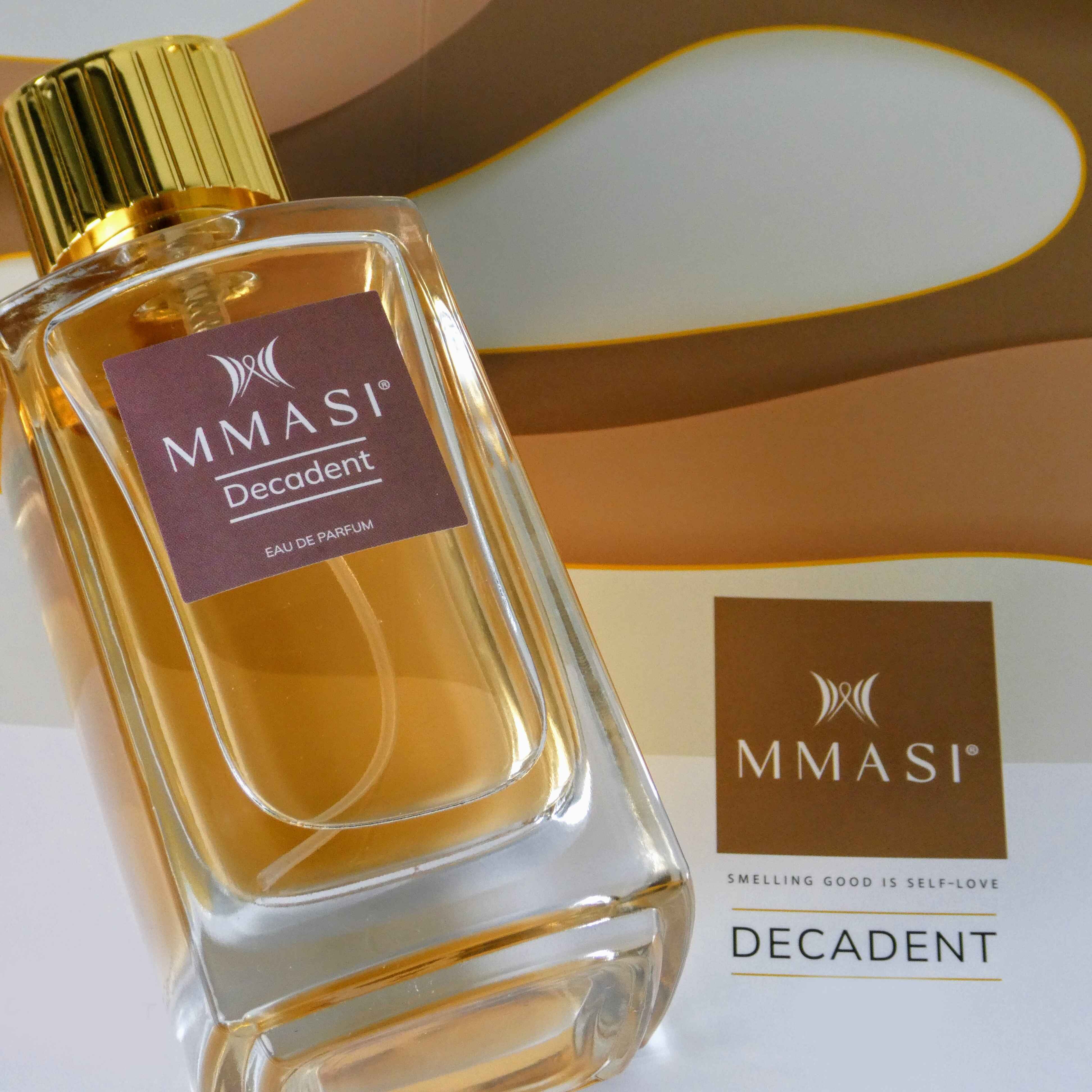 A bottle of MMASI Decadent eau de parfum with a gold cap, placed against a geometric pink and brown background with "MMASI SMELLING GOOD IS SELF-LOVE" written below.