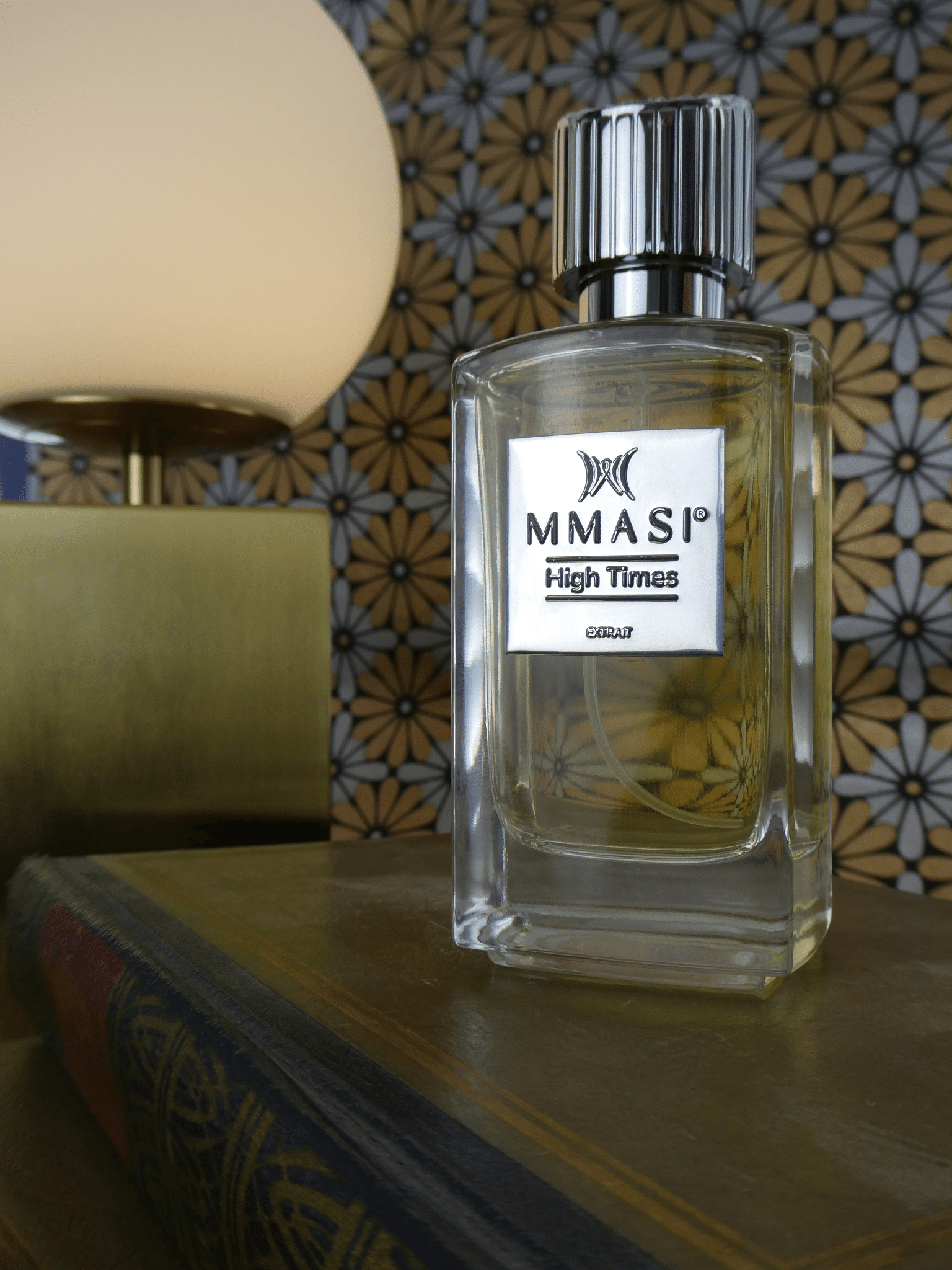 A perfume bottle labeled "MMASI High Times" on a wooden surface with a lamp and patterned wallpaper in the background.